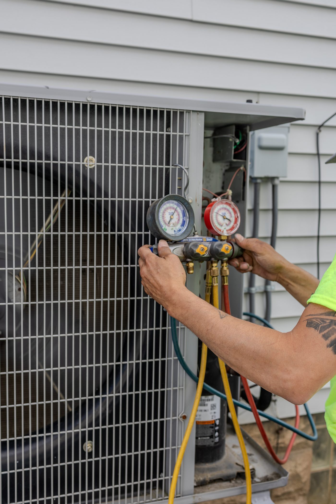 A Hertel technician checking refrigerant pressures with manifold gauges on a condenser