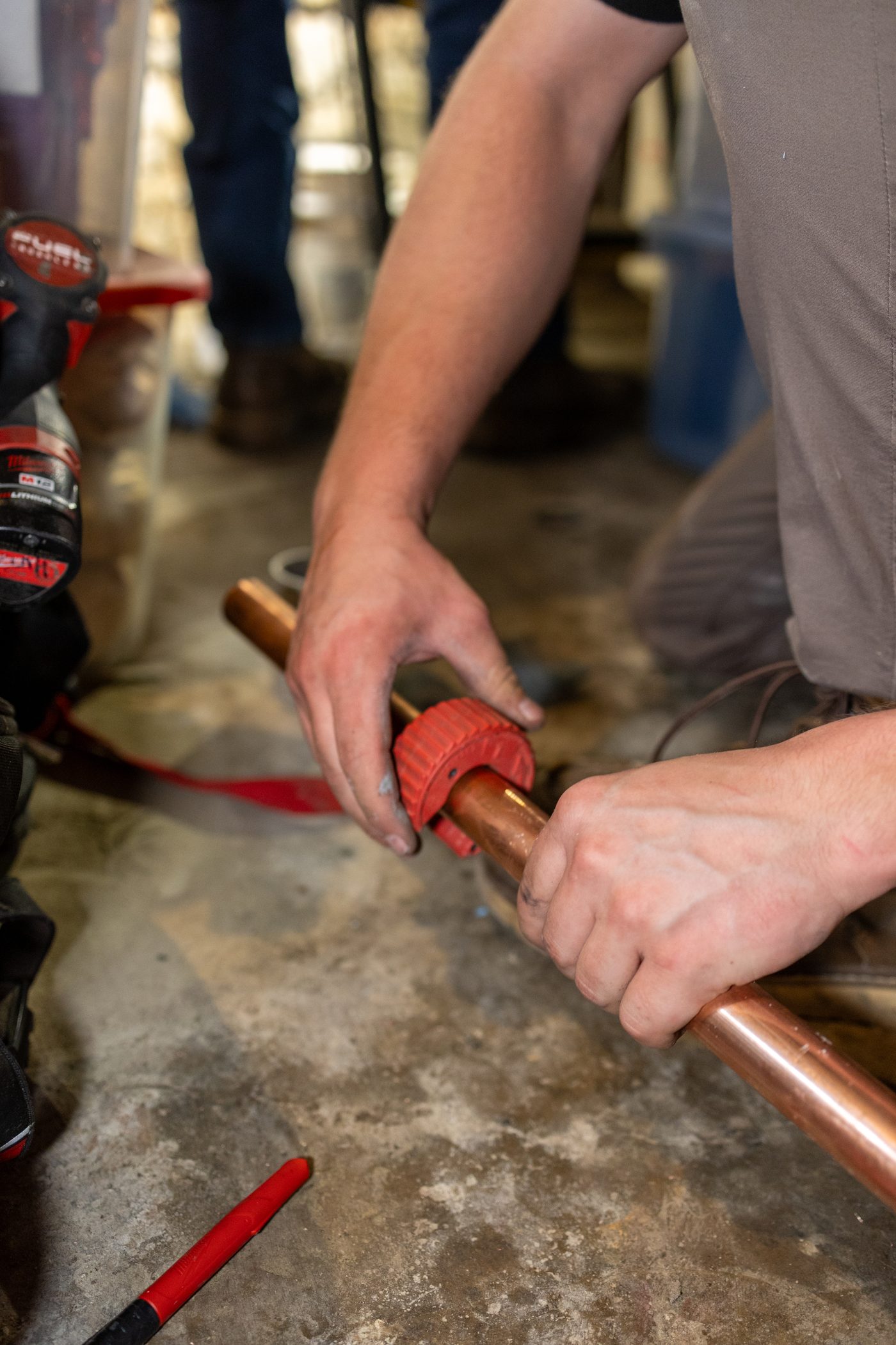 A Hertel plumber cutting copper pipe with a tube cutter