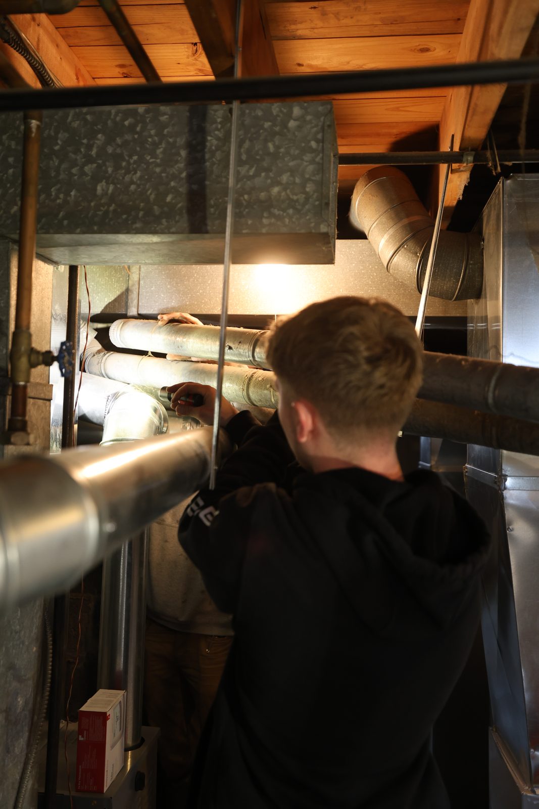 A Hertel technician inspecting ductwork in a basement.
